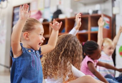 Children raising hands eagerly in a classroom.