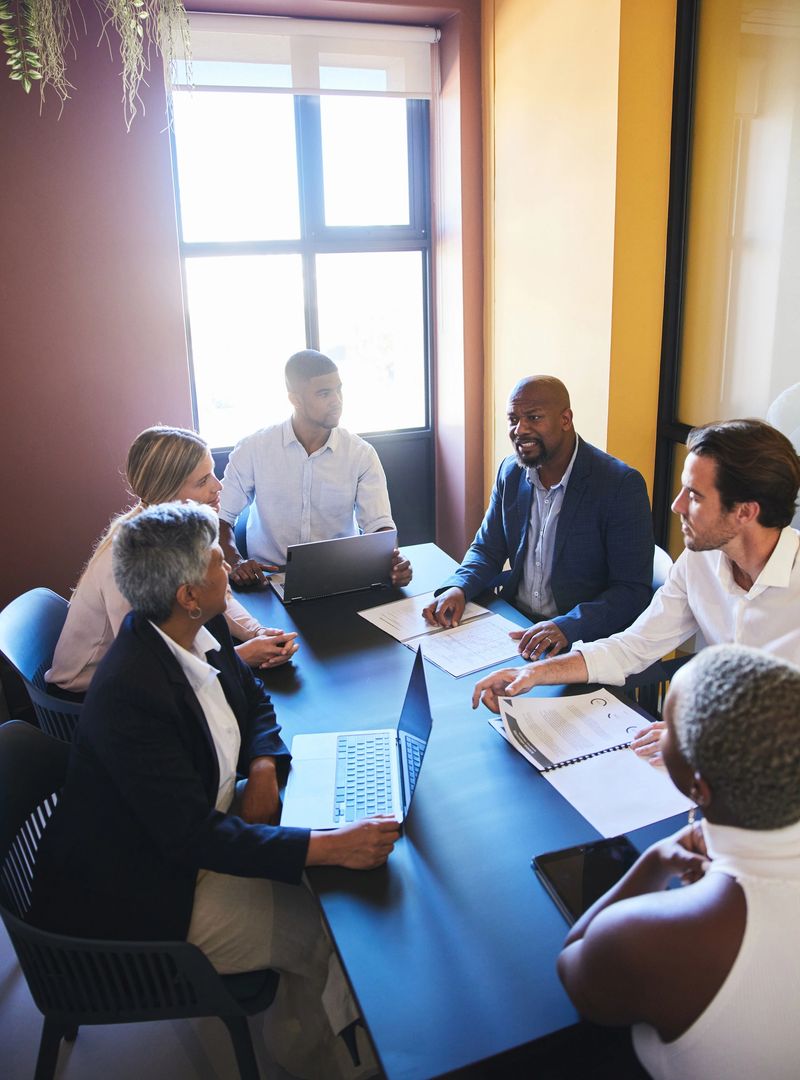 Mature businessman speaking with a diverse group of coworkers during a meeting together around a table in a modern office