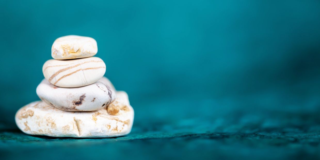 Stack of four smooth white stones on a teal surface.