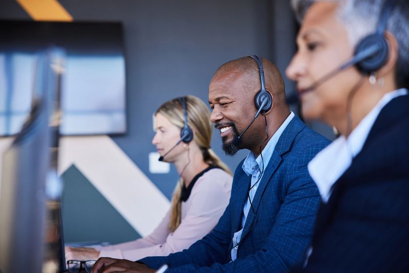 Diverse group of smiling customer service representatives wearing headset working at computers in a modern office