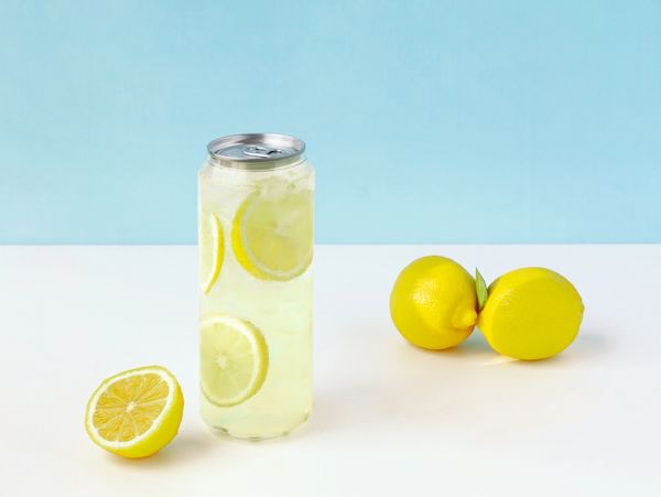 Can of lemonade with lemons on white table.