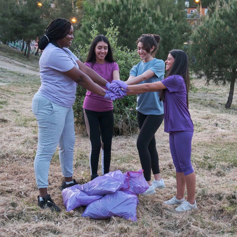 Group of multiracial active women putting their hands together after picking up trash in nature. Plogging concept.
