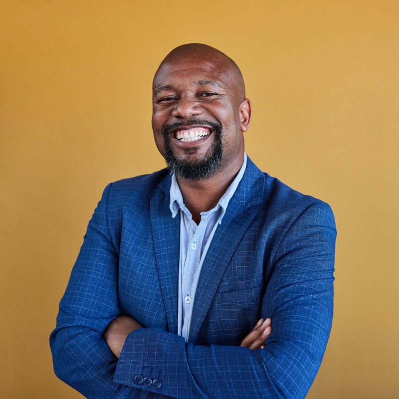 Portrait of smiling mature African businessman wearing a blazer standing with his arms crossed in front of a yellow background
