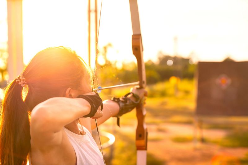 young female archer, archery, shoot arow with bow in nature field to target, success concept, at field for sport exercise at sunset time