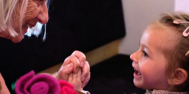 An elderly woman and a young girl share a joyful moment holding hands.