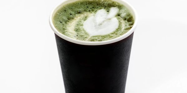 A cup of matcha latte with latte art in a black cup.
