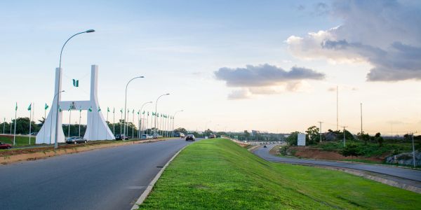 A wide road with Nigerian flags and a white monument.