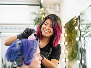 Hairdresser coloring client's hair with vibrant dye.