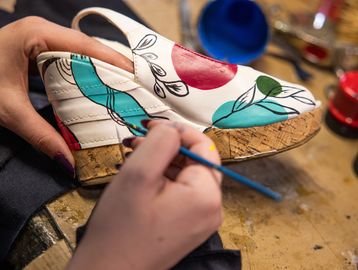 Hand painting a white sandal with colorful floral designs.