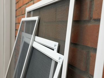 Several window screens leaning against a brick wall.