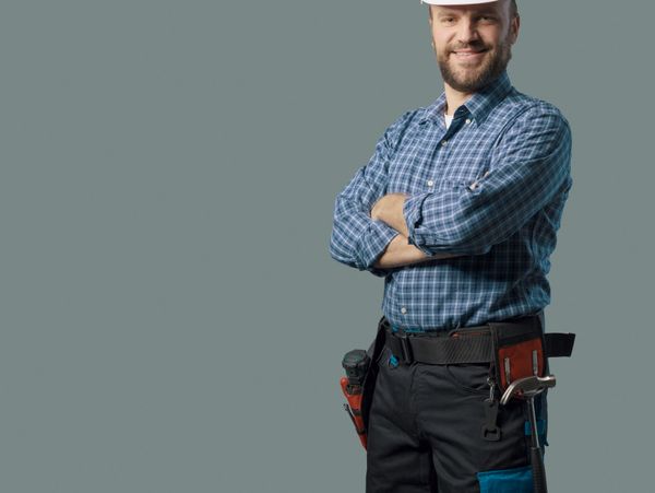 Confident construction worker in a hard hat and tool belt smiling with arms crossed.
