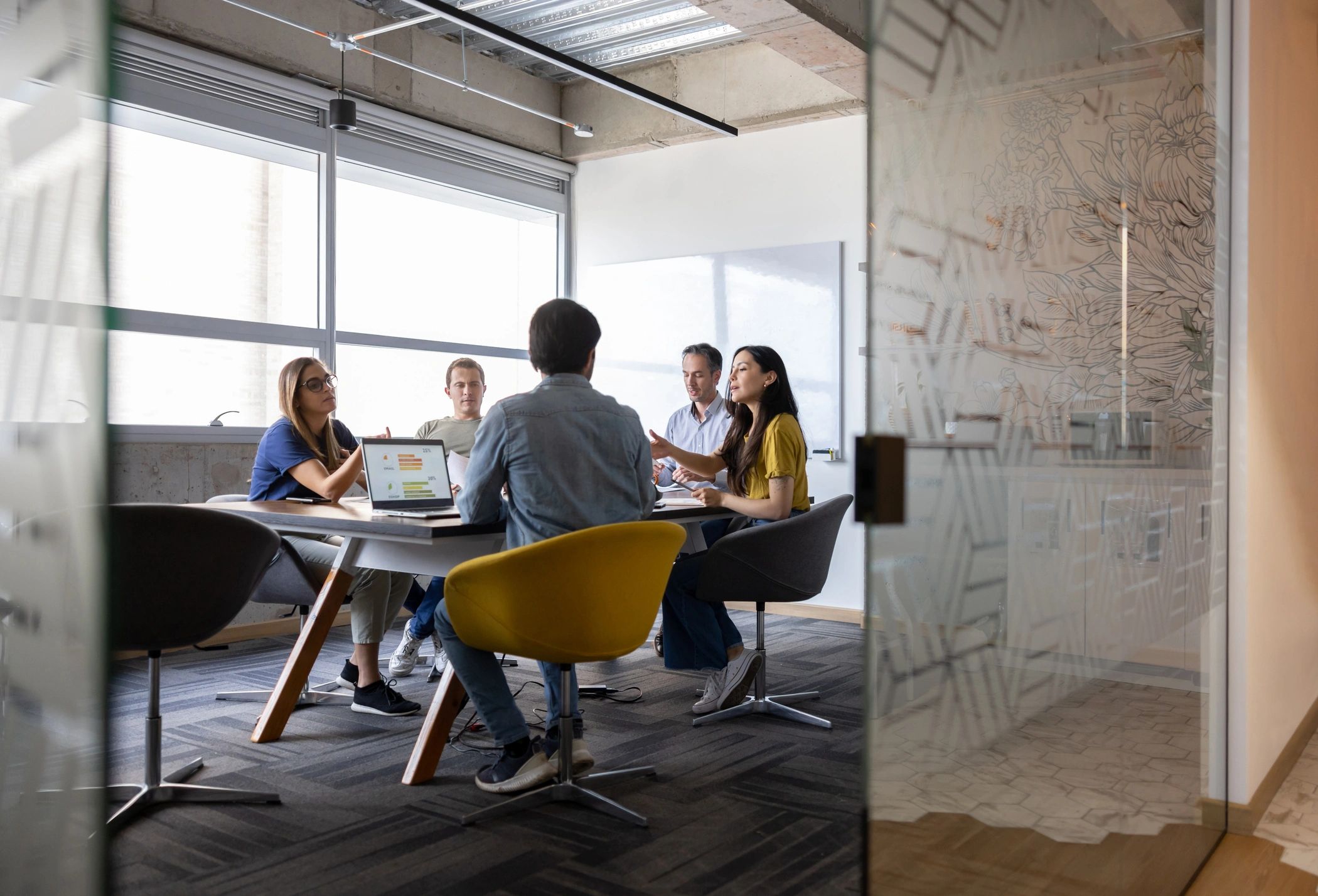 Team meeting in a modern office with laptops and discussions.