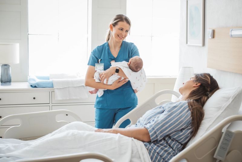 Nurse bringing newborn baby to his mother at hospital bed. They are happy and healthy.