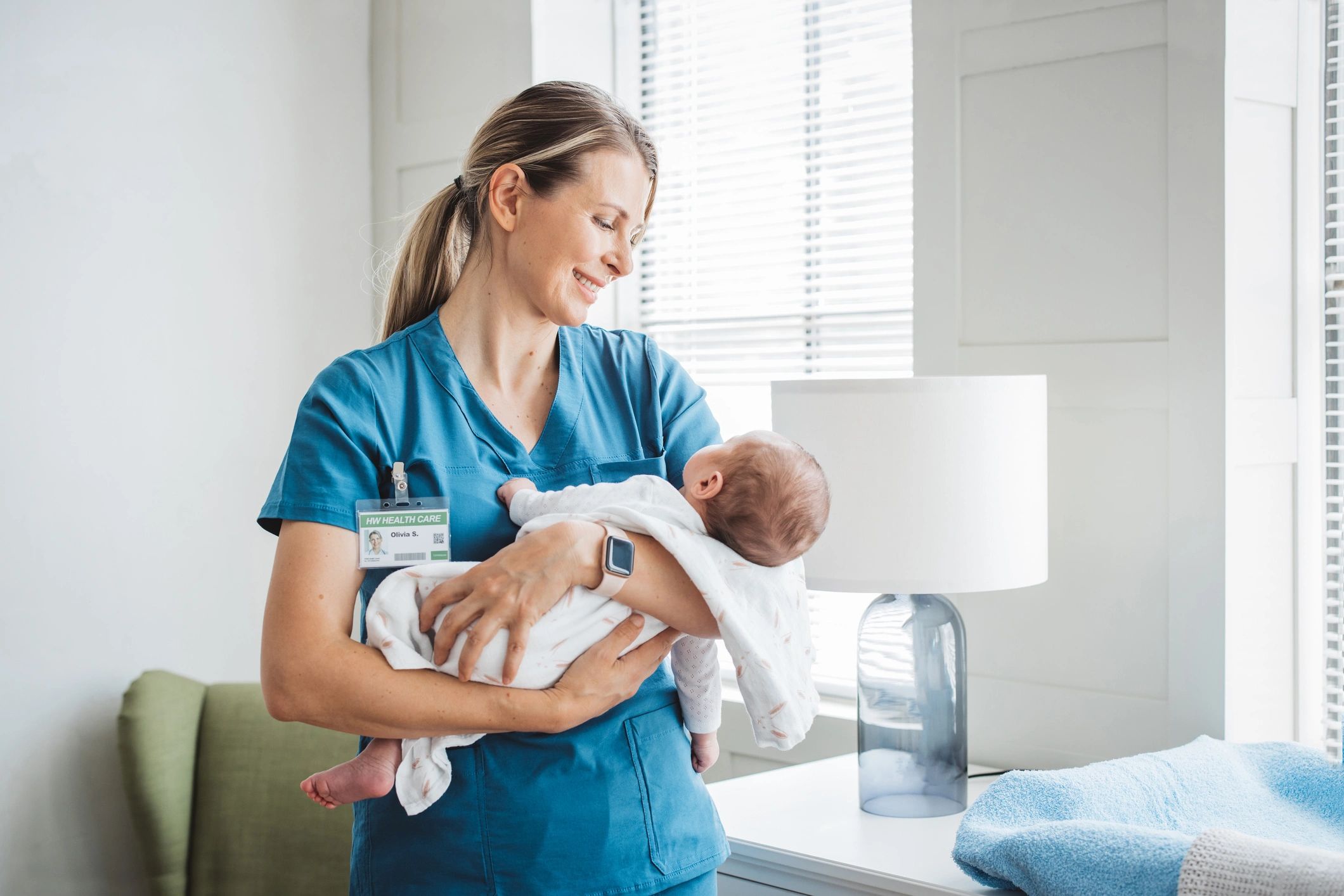 Nurse holding a newborn baby in a bright room.