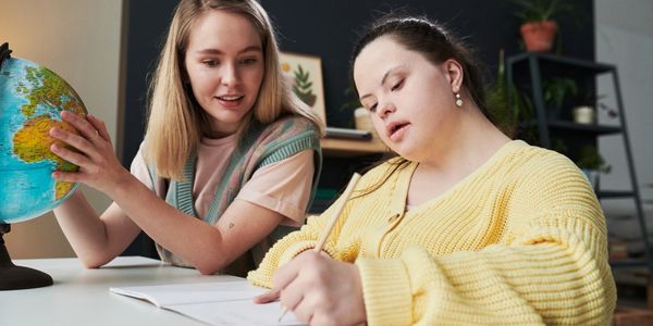 Two women studying with a globe and notebook on a table.