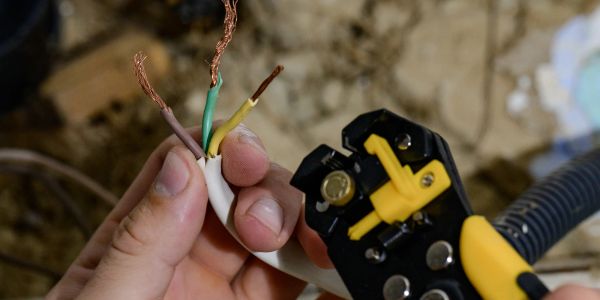 Hand holding stripped electrical wires near a wire stripper tool.