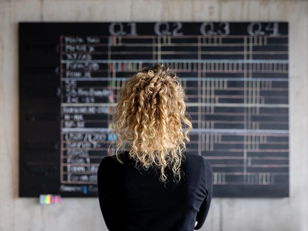 Person with curly hair studying a large blackboard filled with charts and data.