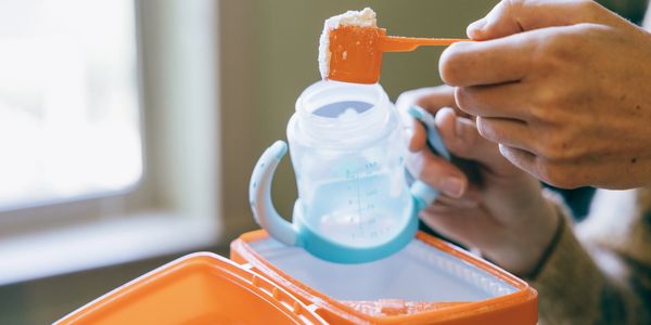 Person scooping baby formula into a bottle.