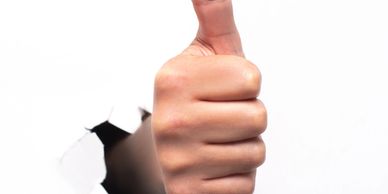 Hand giving a thumbs-up through torn white paper.