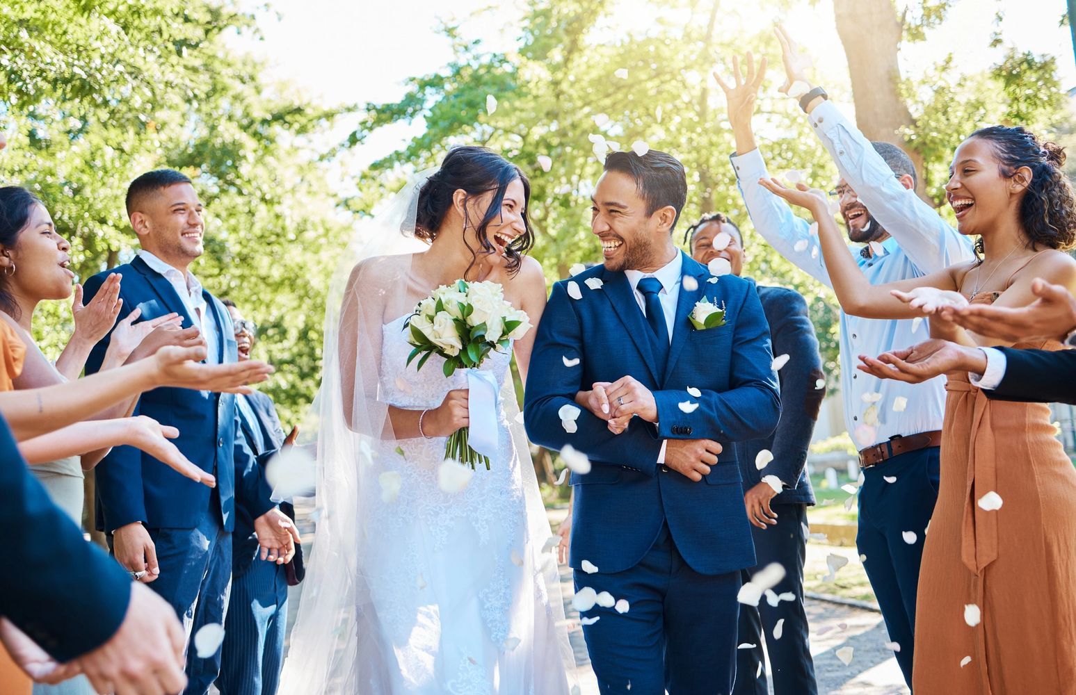 Joyful bride and groom celebrate with friends throwing petals outdoors.