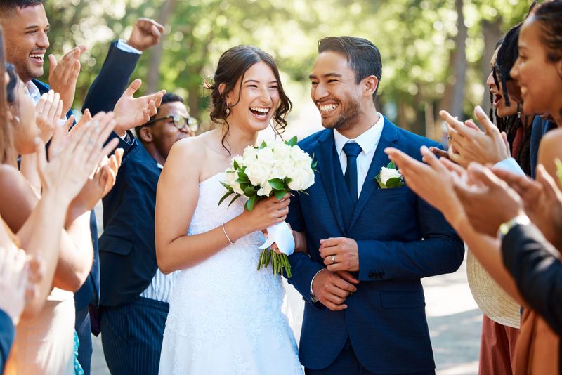 Wedding guests clapping hands as the newlywed couple walk down the aisle. Joyful bride and groom walking arm in arm after their wedding ceremony