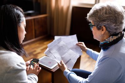 Two women reviewing bills and using a calculator at home.