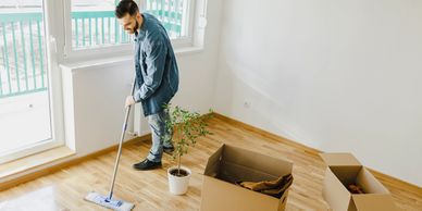 Man cleaning floor in empty room with boxes.