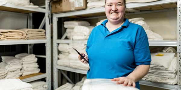 Smiling worker in blue shirt organizing folded linens in a storage room.