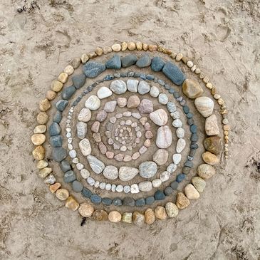 Spiral pattern made of various colored stones on sand.