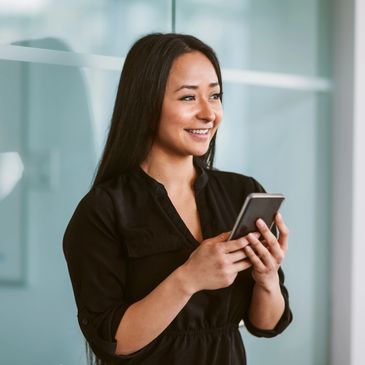 Smiling woman holding smartphone in a modern office setting.