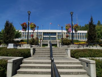 City hall with steps, lampposts, and colorful hanging flowers under a clear blue sky.