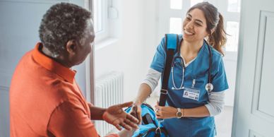 A nurse warmly greeting an elderly man at his home.
