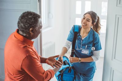 A nurse warmly greeting an elderly man at the door.