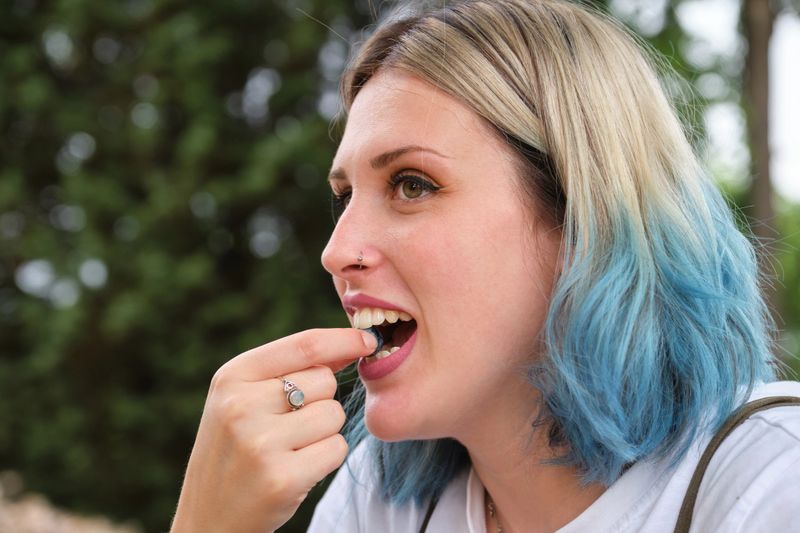 Young happy woman eating a blueberry in a park. Picnic on a sunny summer day.