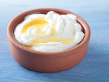 Creamy yogurt with honey in a clay bowl on a blue surface.