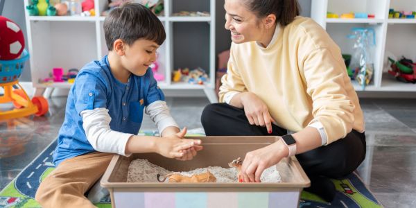 Child and woman play with sand and toys indoors.