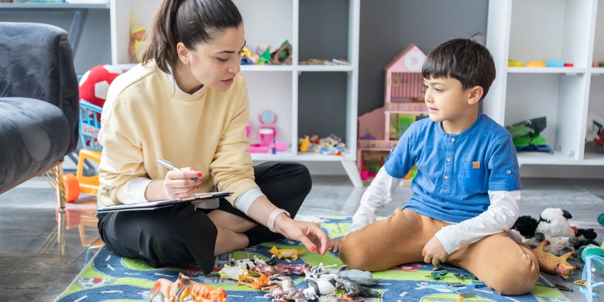 Woman and boy playing with animal toys on the floor.
