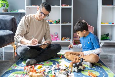 Father and son playing with toys on a colorful rug indoors.