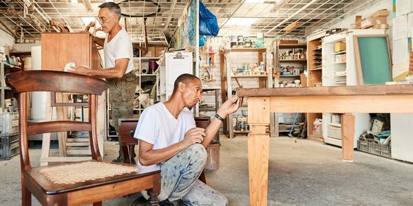 Two men working on wooden furniture in a workshop.