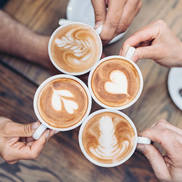 Four hands holding cups of coffee with latte art.