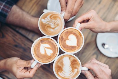Four cups of latte art coffee held together in a toast.