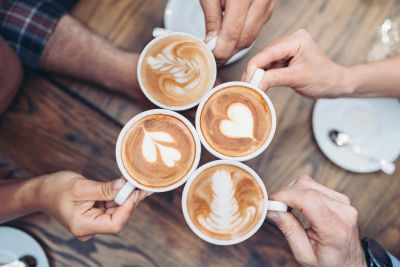 Four people toast with coffee cups featuring latte art.