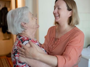 A young woman warmly embraces an elderly woman indoors.