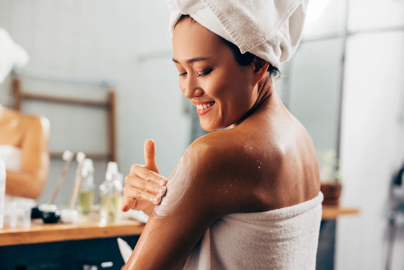Young Asian woman following her skin care routine, she is applying the cream after a shower.
