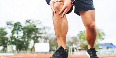 Athlete holding knee in pain on a running track.