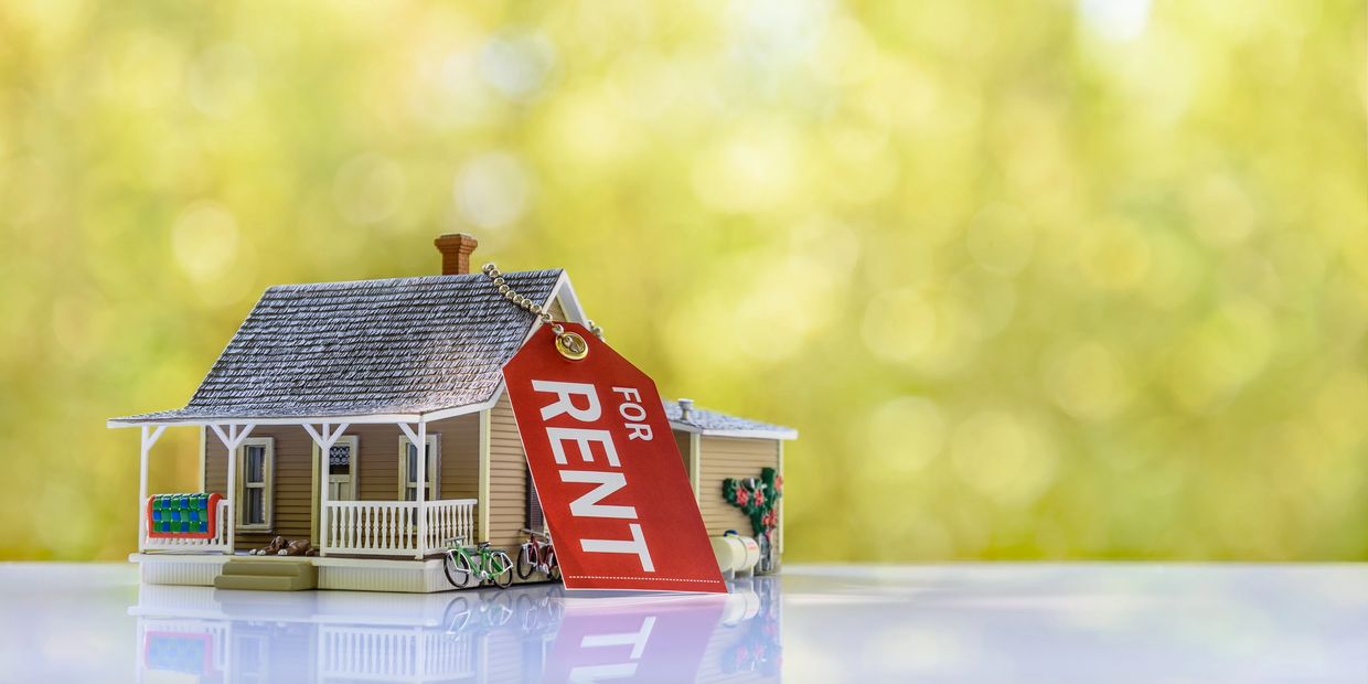 Miniature house with a large red "For Rent" tag on a reflective surface.