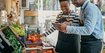 Two men sorting fresh tomatoes at a grocery store.