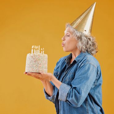 Woman in party hat blowing out candles on birthday cake.