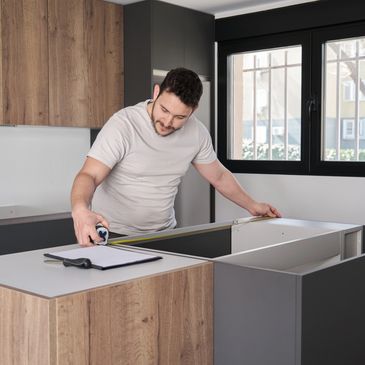 Man measuring kitchen island with tape measure during renovation.