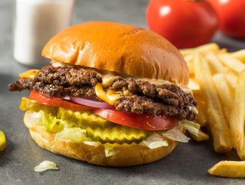 A cheeseburger with lettuce, tomato, pickles, and fries on the side.